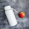 A drink bottle in white with a straw, positioned next to a red apple on a textured grey surface.