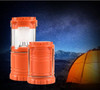 An orange camping lantern set against a starry night sky, with a tent in the background. One lantern is larger than the other.