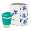 A drink bottle with a teal silicone sleeve and a gold base, next to a decorative box featuring leaf designs.