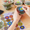 A hand holding a salad container with a glossy sticker. A sticker sheet featuring colourful circular designs is beside it.
