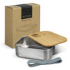 A stainless steel lunch box with a wooden lid, grey strap, and packaging in natural tones.