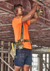 A man wearing an orange shirt and navy blue cargo shorts works on a construction site, using a power drill.