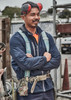 A man in a navy blue packable rain jacket stands with arms crossed, wearing earmuffs and a safety harness.