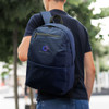 A navy blue backpack with a logo, carried by a person outdoors among trees.