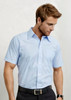A short sleeve, button-up shirt in light blue with a single pocket and a logo on the chest.