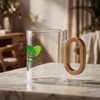 A glass coffee cup with a bamboo handle and a green logo, placed on a marble surface with a soft background.