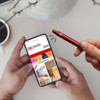A red NFC Directview Stylus Pen held by a hand, alongside a smartphone displaying a website, on a table.