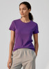 A purple women's short sleeve tee displayed on a model, paired with grey pants. The tee features a simple design and branding.