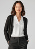 A woman models a black knit cardigan over a white blouse, paired with tailored black trousers. The cardigan has buttons and a subtle texture.