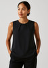 A sleeveless black blouse featuring pleat details, modelled by a woman with her hands in pockets.