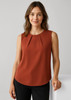 A sleeveless blouse in rust colour featuring pleat detail, modelled by a smiling woman. The background is neutral.