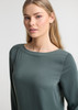 A women's boatneck top in green, featuring long sleeves and a smooth fabric. The design includes a subtle brand logo.