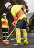 High-visibility yellow and orange work pants with reflective tape, worn by a man sweeping the road, alongside a woman in similar attire.