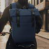 A navy blue soft-touch flap backpack with adjustable straps and a front pocket, worn by a person on a bicycle.