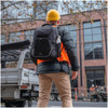 A black High Sierra Access 4.0 backpack rests on the back of a person wearing a hard hat and bright orange vest.
