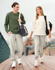 A man in a green sweatshirt and grey sweatpants walks alongside a woman in a white sweatshirt and grey sweatpants, both carrying bags.