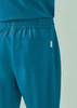 A pair of teal unisex scrub pants featuring an elastic waistband and a back pocket. Branding is visible.