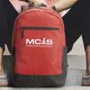 A red and black backpack is resting on steps, featuring a logo on the front.