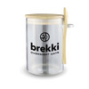 A clear overnight oats container with a wooden lid and spoon, featuring a logo on the side.