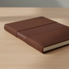 A brown notebook with a textured cover, featuring elastic bands on the front, placed on a wooden surface.