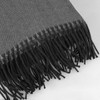 A grey herringbone throw blanket with decorative fringes along one edge, featuring a subtle texture.