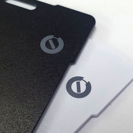A carbon Bluetooth tracker featuring a black and a white side, both with branding logos.