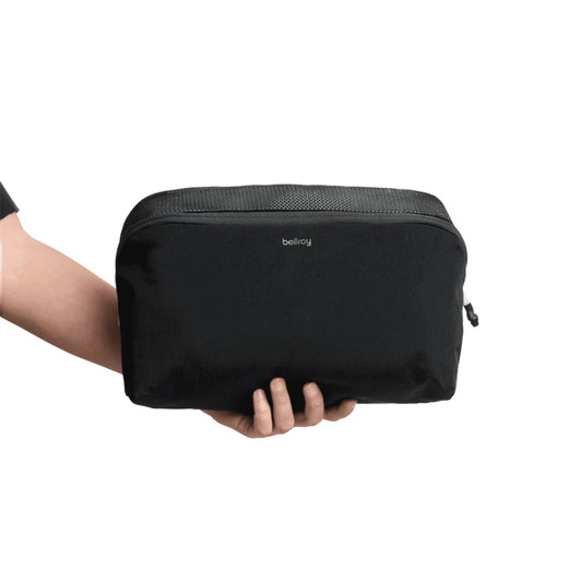 A black packing cube held in a hand, featuring a mesh panel and branded logo.
