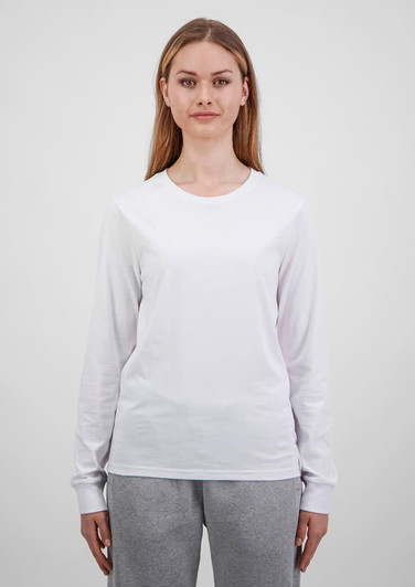 A woman wears a white long sleeve tee, paired with grey trousers. The tee features a simple design and has a logo.