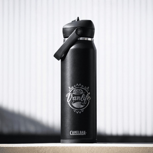 A drink bottle in matte black with a flip straw lid and a logo featuring a vanlife theme.