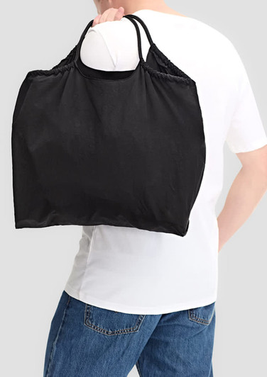A black nylon tote bag is being carried over the shoulder by a person wearing a white shirt and blue jeans.