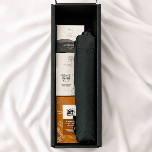 A black umbrella and snack items in a rectangular box on a soft surface.