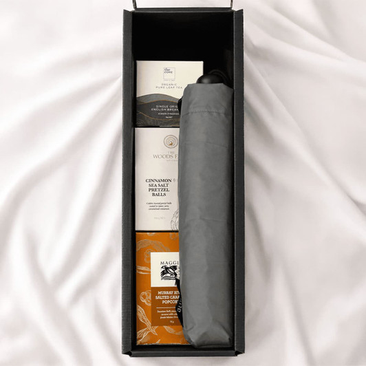A grey umbrella nestled in a black box alongside snack items, including pretzel balls and popcorn.