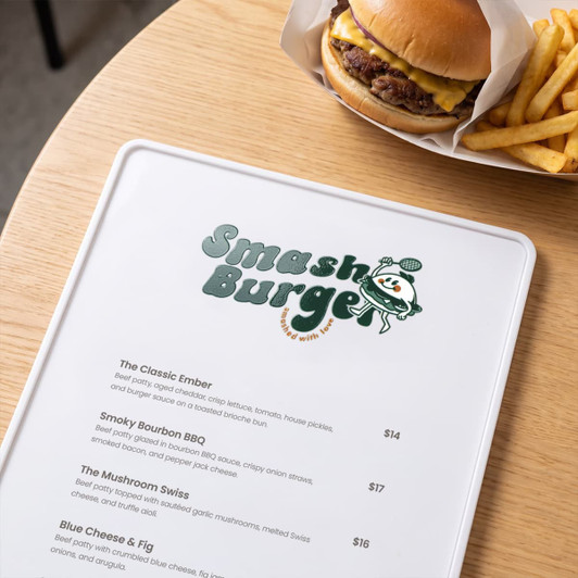 A menu on a wooden table featuring various burger options alongside a cheeseburger and fries in the background.