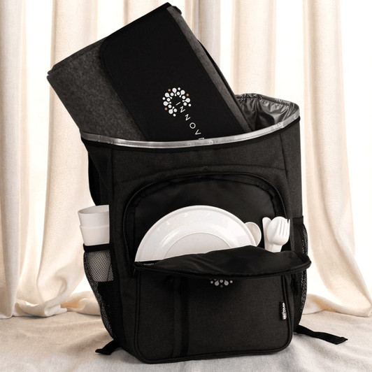 A black picnic backpack with a grey blanket, plates, cutlery, and a drink bottle in external pockets.