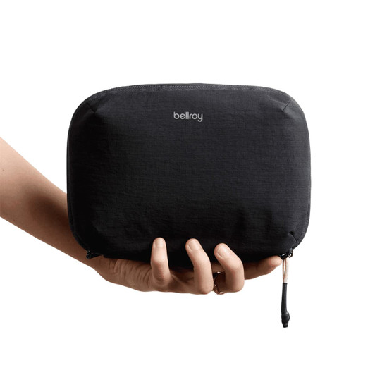 A hand holding a black tech kit with a smooth texture and a logo. The zippered pouch is compact and sleek.