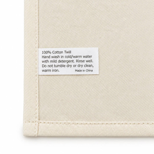 A cream cotton tea towel featuring a care label with washing instructions and a brand logo.