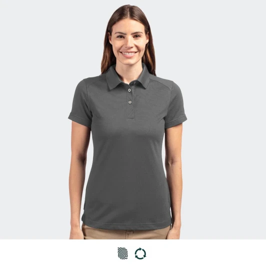 A women's polo shirt in dark grey, featuring a collar and logo. The model is smiling and facing forward.