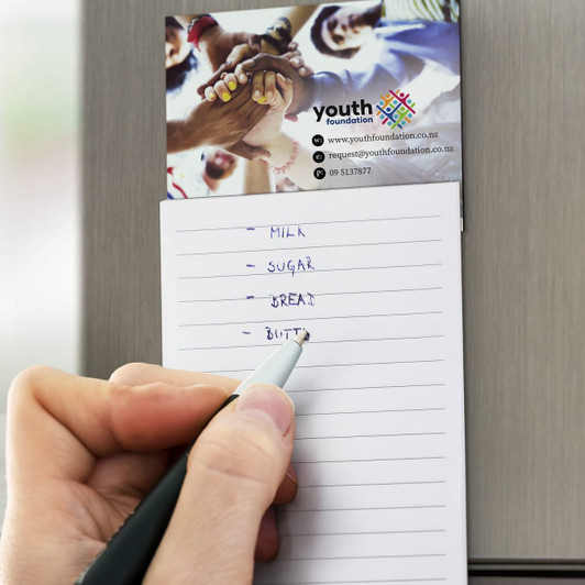 A lined magnet pad with a pen writing a shopping list, featuring a colourful logo at the top.