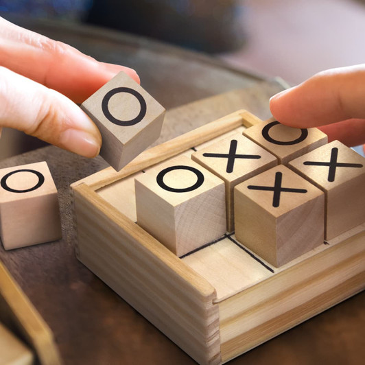 A wooden Tic Tac Toe game with light timber blocks featuring O and X marks, housed in a small timber box.