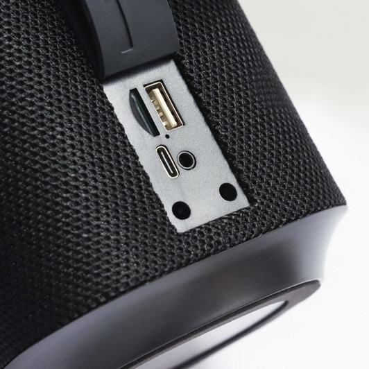 A close-up of a black Bluetooth speaker, highlighting USB and USB-C ports on its textured surface.