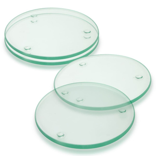 A set of four round glass coasters in pale green, featuring subtle raised dots for stability.