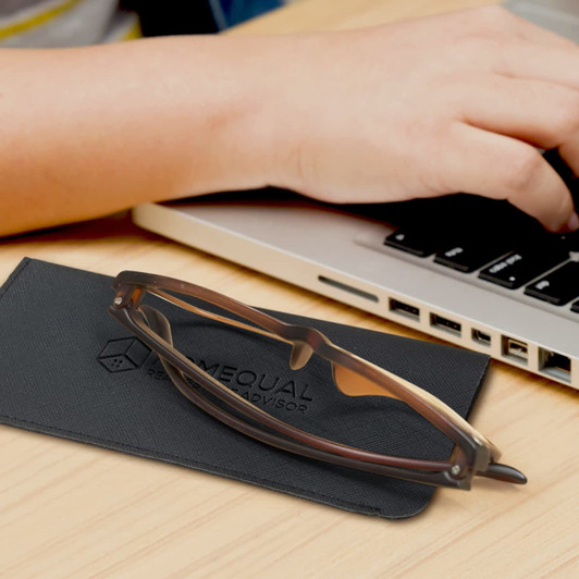 A brown Essex sunglass pouch with a pair of sunglasses resting on top, next to a laptop on a wooden surface.