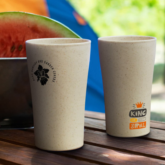 A set of natural-coloured plastic tumblers with a logo and a playful graphic, placed on a wooden table.