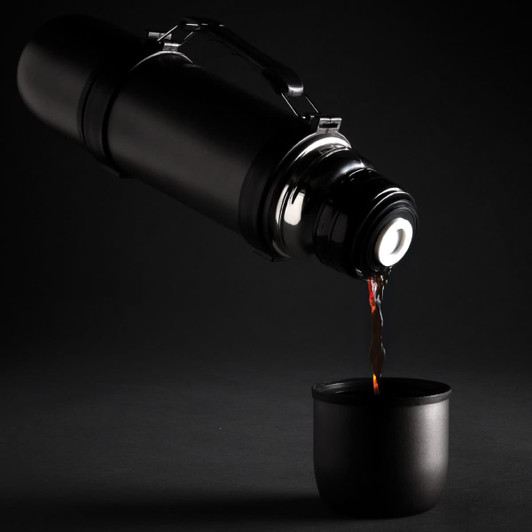 A drink bottle in matte black pours liquid into a matching cup, showcasing a sleek vacuum flask design with a handle.