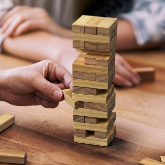 A wooden Mini Tumbling Tower with multiple layers, featuring light and dark wood blocks on a tabletop.