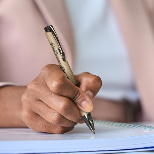 A hand holding a beige and silver pen, poised above a notepad, ready for writing. The pen features a logo.