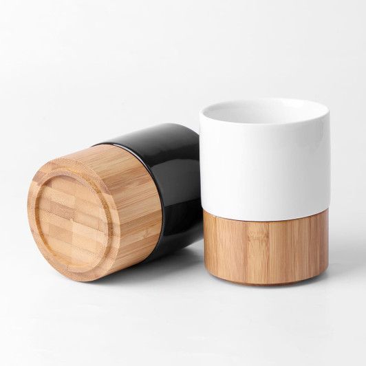 A black ceramic mug with a bamboo base and a white ceramic mug with a bamboo base, displayed together.