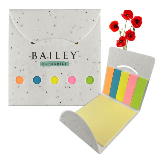 A sticky note pad with pastel-coloured notes in a grey, speckled holder, accompanied by artificial red corn poppies.