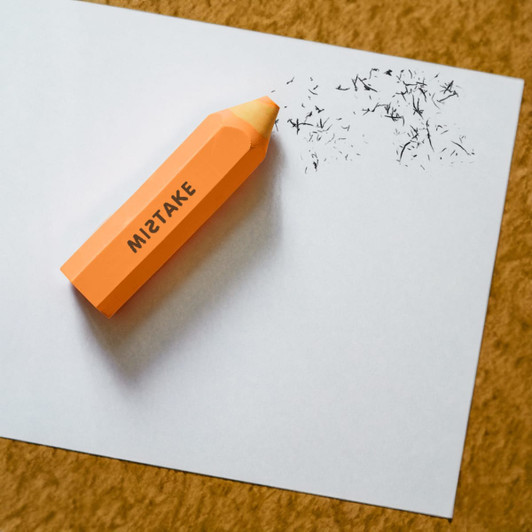 An orange pencil-shaped rubber eraser lying on a sheet of paper with pencil shavings nearby.