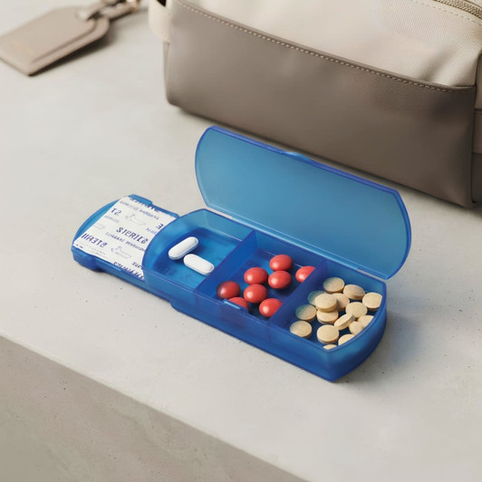 A blue travel pill box with compartments containing various pills, resting on a flat surface beside a bag.